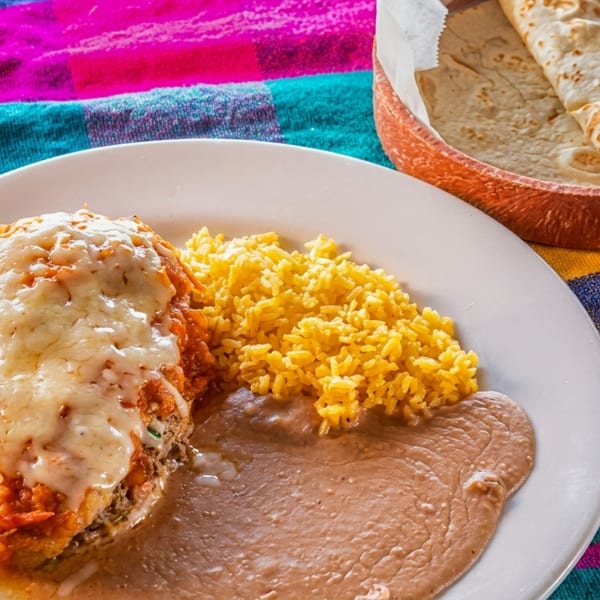 A plate of Mexican food with a chile relleno, yellow rice, refried beans, and a basket of tortillas.