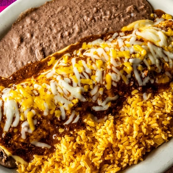 A plate of Mexican food with a burrito covered in cheese and sauce, rice, and refried beans.