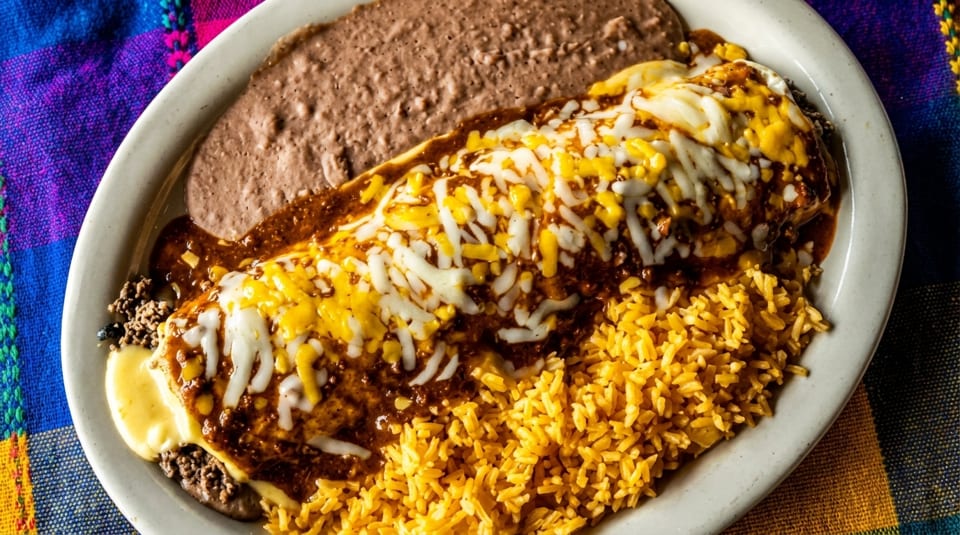 A plate of Mexican food with a burrito covered in cheese and sauce, rice, and refried beans.